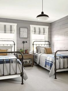 two twin beds in a bedroom with gray walls and white bedding, one has a plaid blanket on it