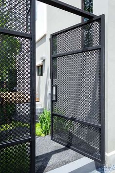 an iron gate is open on the side of a white building with plants in it