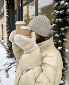 a woman holding a cup of coffee in front of a building with snow on the ground