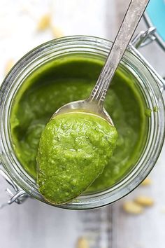 a spoon full of green pesto sitting in a jar