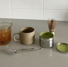 there is a cup and spoon on the counter next to two cups with green tea in them