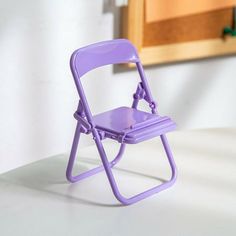 a purple plastic folding chair sitting on top of a white table next to a wooden cabinet