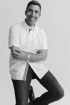 a man sitting on top of a stool with his arms crossed and smiling at the camera