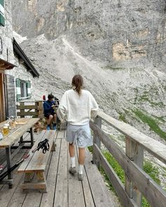 a woman standing on top of a wooden deck next to a building and mountains in the background