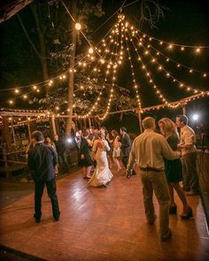 a group of people standing on top of a wooden floor next to a forest filled with lights