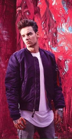 a young man standing in front of a red tree with his hands in his pockets