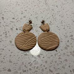 two brown earrings are sitting on a white counter top, one is shaped like a circle and the other has a knot at the end