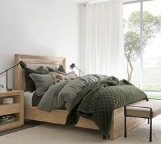 a bed with green comforter and pillows in a room next to a large window