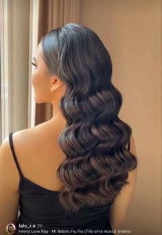 a woman is looking out the window with long hair in her hand and wearing a black top