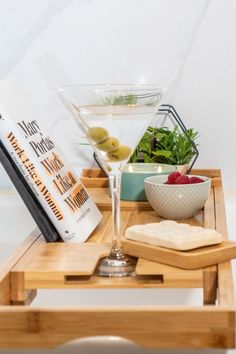 a wooden tray topped with a martini glass and other food on top of it next to a book