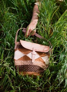 a woman's hand holding onto a brown and white purse in some tall grass