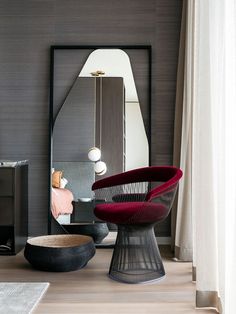 a chair and mirror in a room with wood flooring, white curtains and grey walls