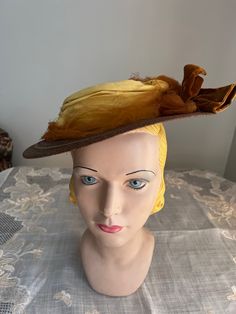 Antique brown  braided straw hat. It has a small round crown and small brim.  Around the crown is a yellow cotton  cloth and rust netting band. On one side is a brown velvet bow. The hat is an oval shape or more egg shape with the fro t being wider.At the back underneath is 2 green and brown silk flower shapes with brown velvet ribbon connecting them.If hat is tipped to one side the rear flowers can be seen but if set straight, they would not be seen very well.  Inside is lined in black fabric and there is an elastic cord. Measurements Inside circumference is about 18 inches Front to back 12 inches Across 10.5 inches  Crown 1.5 inches high Brim is 3.5 inches in the front and about 2 inches in the back. Condition - good   Brown straw is good and yellow cloth band is good. Rust netting is to Vintage Brown Hat Band For Kentucky Derby, Vintage Brown Hat Bands For Kentucky Derby, Vintage Brown Top Hat For Costume, Brown Vintage Top Hat For Costume, Victorian Cloche Hat For Vintage Events, Vintage Hats For Kentucky Derby And Country Events, Vintage Brown Hat Bands For Country Events, Victorian Costume Hat With Curved Brim, Victorian Adjustable Cloche Hat