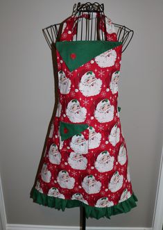 a red apron with santa clause on it and green trim around the waist, hanging from a metal rack