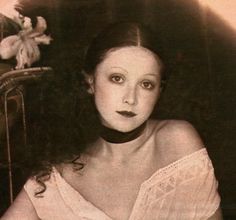 an old photo of a woman wearing a white dress and posing for the camera with flowers in her hair