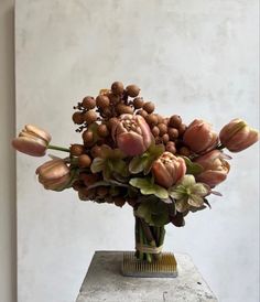 a vase filled with lots of flowers sitting on top of a cement block in front of a white wall