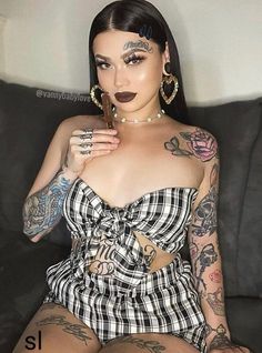 a woman with tattoos on her body sitting on a couch and posing for the camera