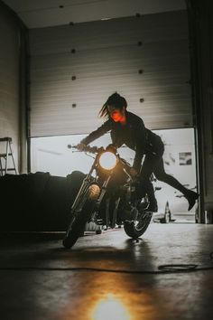 a man riding on the back of a motorcycle in a garage with red light coming from behind him