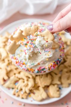 a hand holding a cookie doughnut with sprinkles on it and some cookies in the background