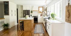 a kitchen with wooden floors and white cabinets, an island countertop and potted plants