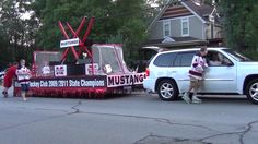 a parade float in the street with people standing on it's sides and cars parked behind it