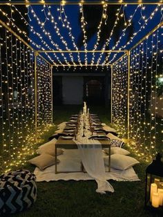 an outdoor dining area is lit up with fairy lights and white tablecloths on the grass