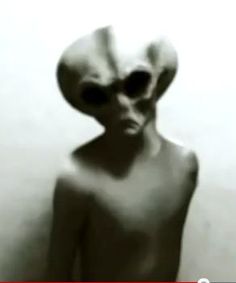 an alien is standing in front of a white wall and looking at the camera man