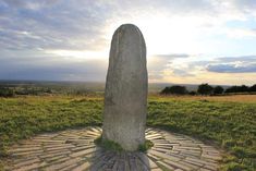 a large stone standing in the middle of a grass covered field with a sky background