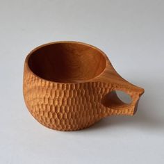 a wooden bowl sitting on top of a white table next to a cup with holes in it