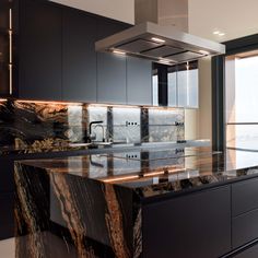 a kitchen with black cabinets and marble counter tops, along with an island in the middle