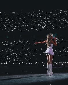 a woman standing on top of a stage with a microphone in her hand and lights behind her