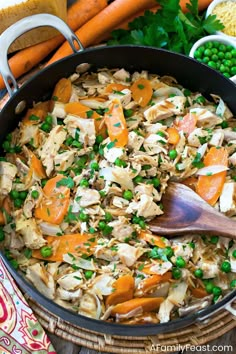 a pan filled with vegetables and meats on top of a table next to carrots