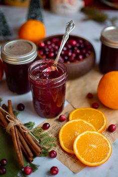 oranges, cinnamon sticks, and jam are on a table with other food items