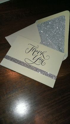 two white envelopes with silver glitter on them and the word thank you written in black ink