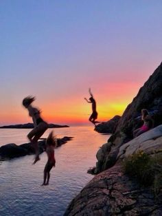 people jumping off rocks into the water at sunset