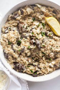 a white bowl filled with rice and mushrooms next to a lemon wedge on a napkin