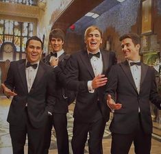 four men in tuxedos are laughing and posing for the camera with their hands together