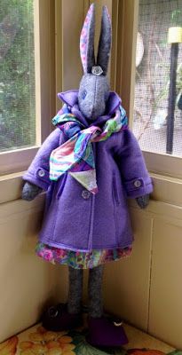 a stuffed animal in a purple coat standing next to a window