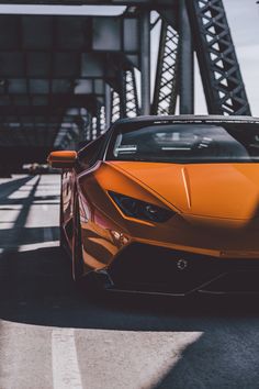 an orange sports car parked in front of a bridge