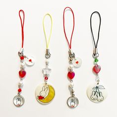 three necklaces with charms attached to them on a white surface, one has a red ribbon and the other has a cartoon character