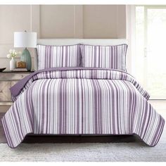 a bed with purple and white striped comforter in a room next to a table