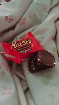 a piece of chocolate sitting on top of a bed next to a bag of reeses