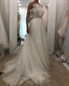 a woman standing in front of a mirror wearing a white dress with ruffles on it