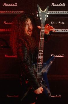 a man with long hair holding a guitar in front of a red and black background