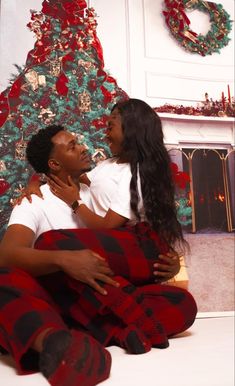 a man and woman sitting on the floor in front of a christmas tree