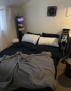 a bed with black sheets and white pillows in a small room next to a window