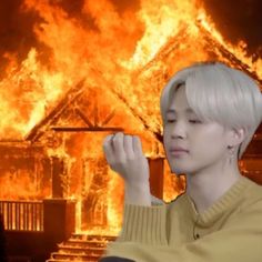 a person sitting in front of a fire with their hands up to their face and the house on fire behind them