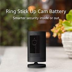 the ring stick up cam battery is sitting on a table next to a potted plant