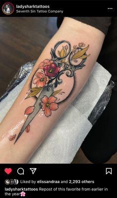 a tattoo on the arm of a woman with scissors, flowers and leaves in it