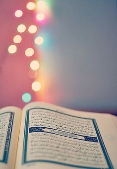 an open book sitting on top of a table next to a christmas tree with lights in the background